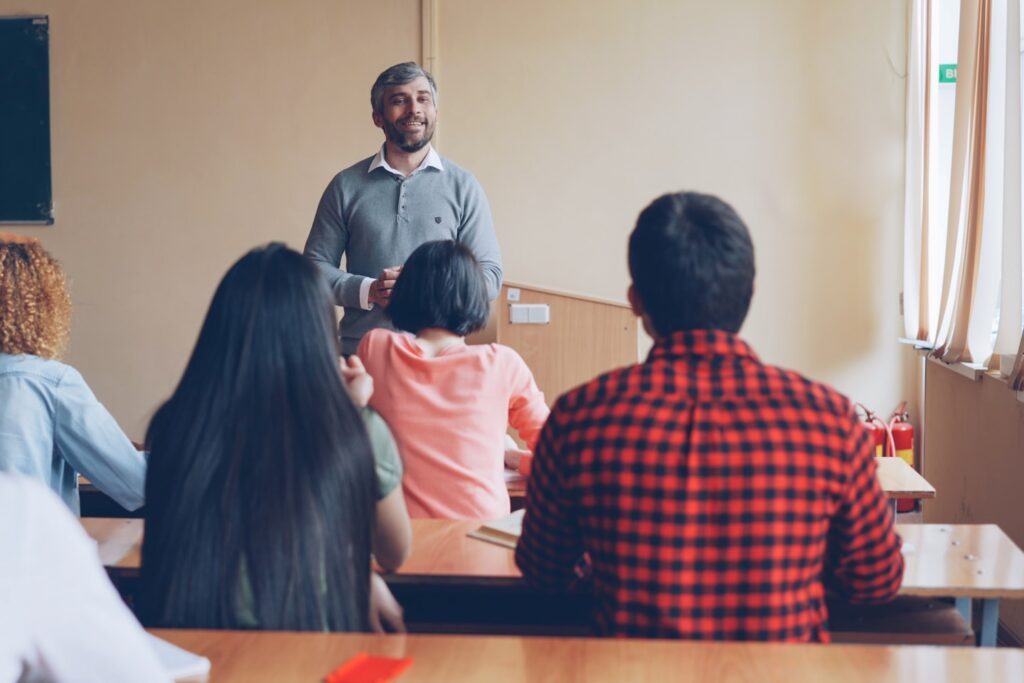 Students listening teacher's answer standing in front of students' desk. Schools and people concept.